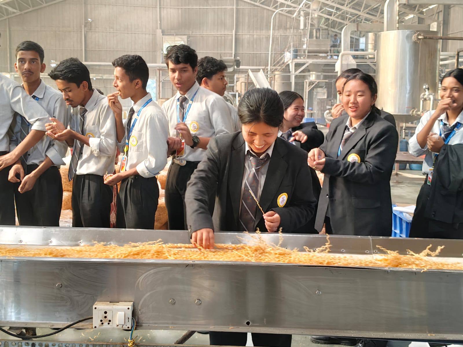 Class XII students at a noodles factory educational visit, examining the production line
